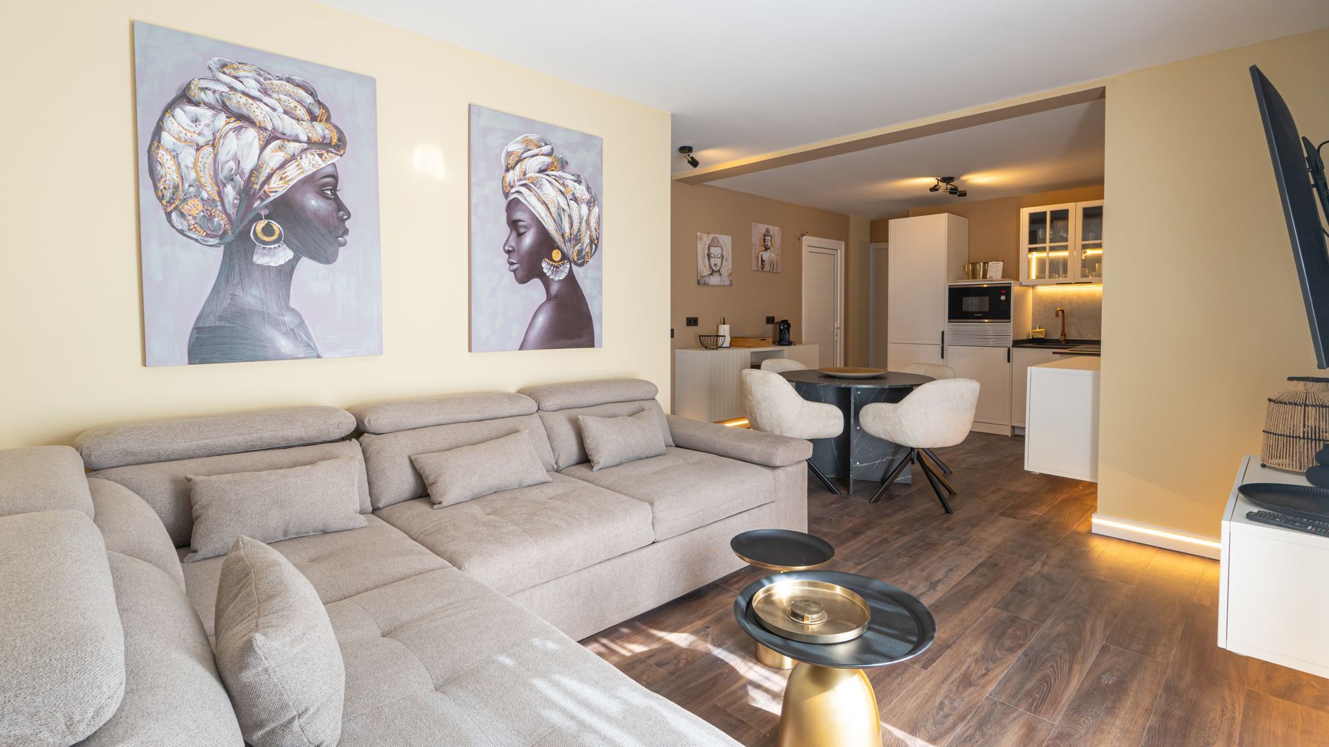 Bright modern living room with a beige sectional, wall art, wood floors, and an open kitchen area