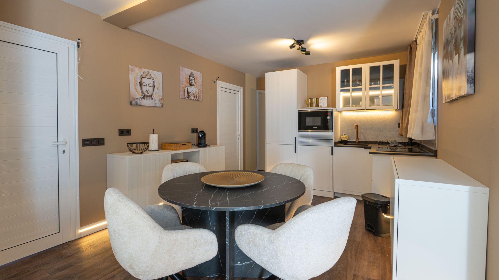 Modern dining and living area with round table, white chairs, and a kitchen in the background