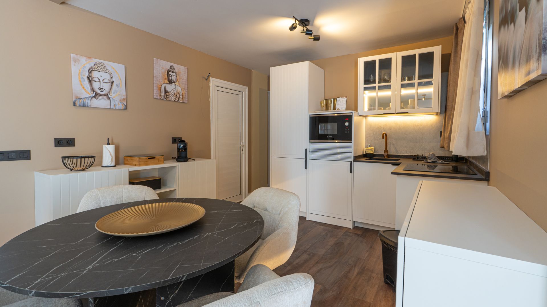 Modern kitchen and dining area with white cabinets, round table, and wall art in warm lighting