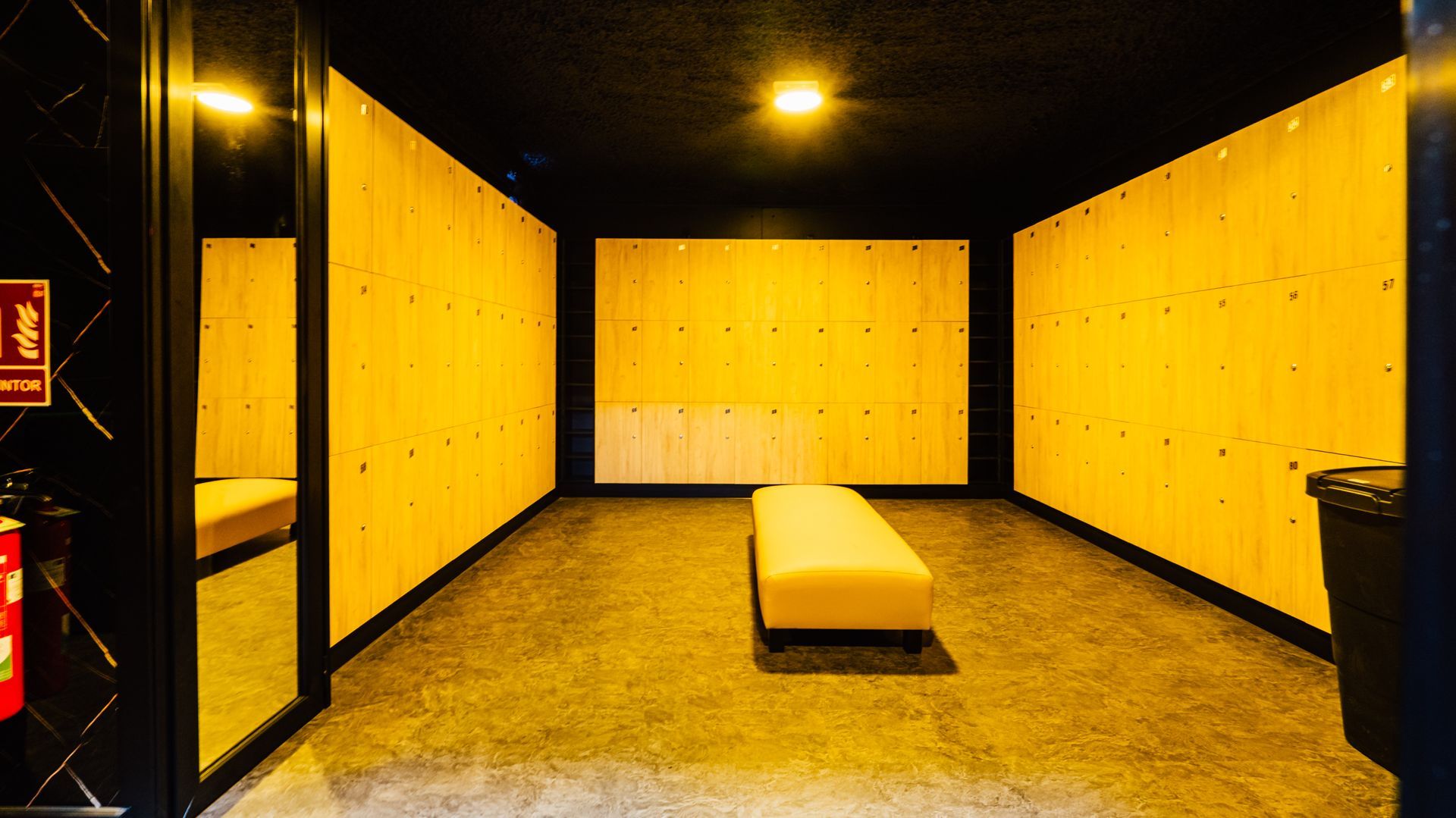Empty room with yellow padded walls, a central bench, and dark ceiling lights