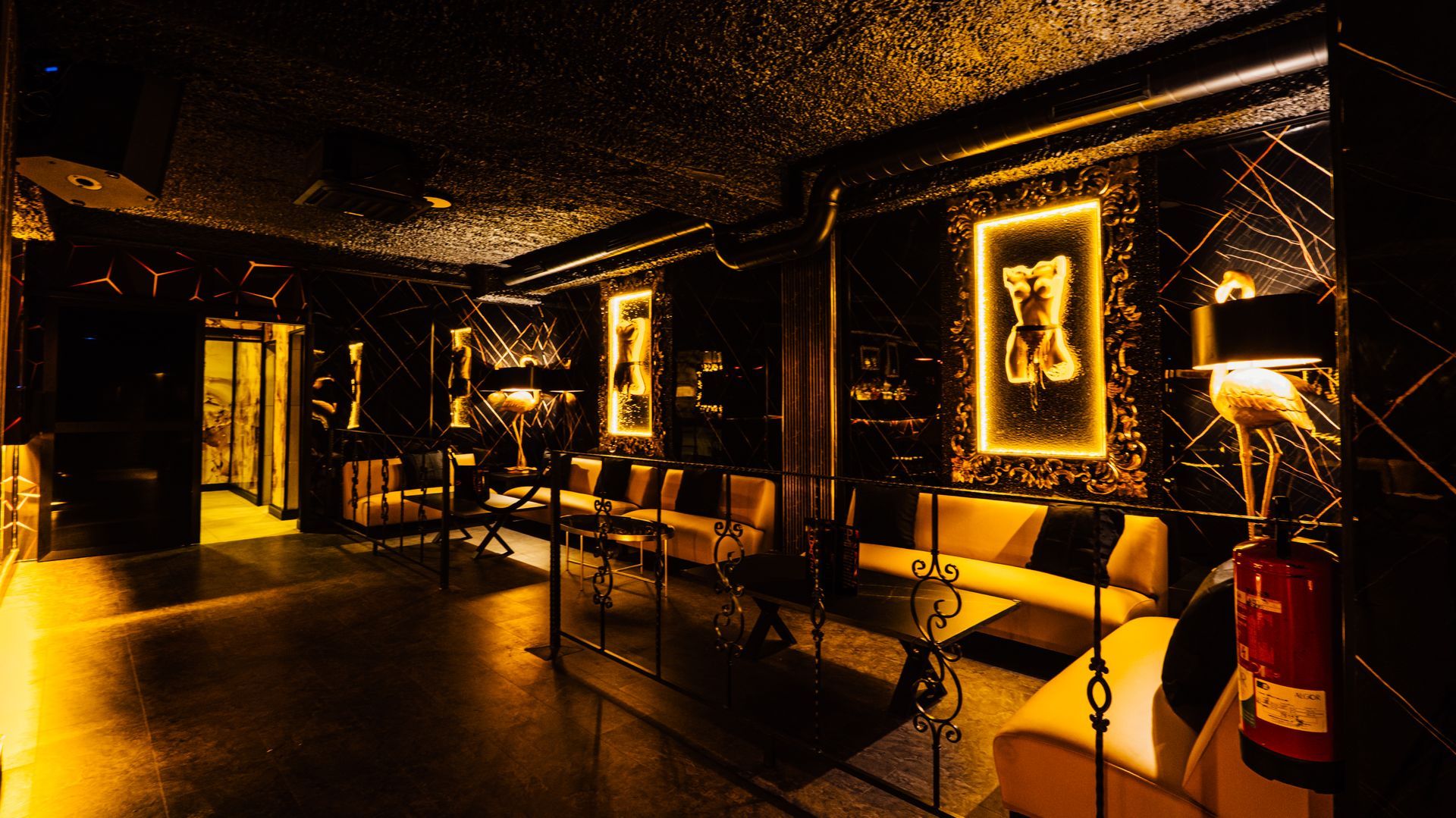 Dimly lit lounge with gold decor, framed portraits, and seating along the walls
