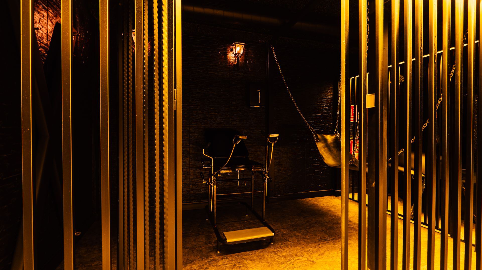 Dimly lit industrial gym with a hanging punching bag, equipment, and metal bars in amber light