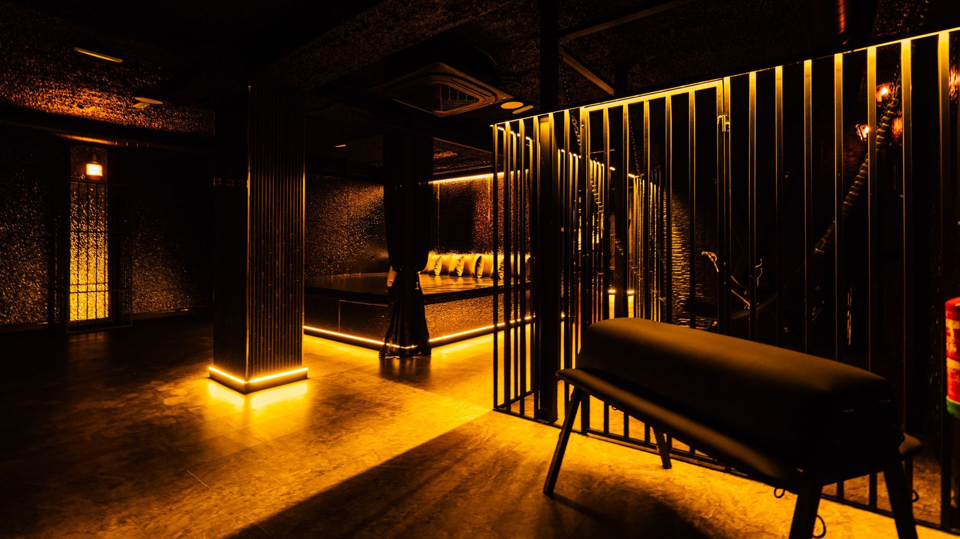 Dim amber-lit lounge with benches, dark wood slats, and warm reflections on the floor