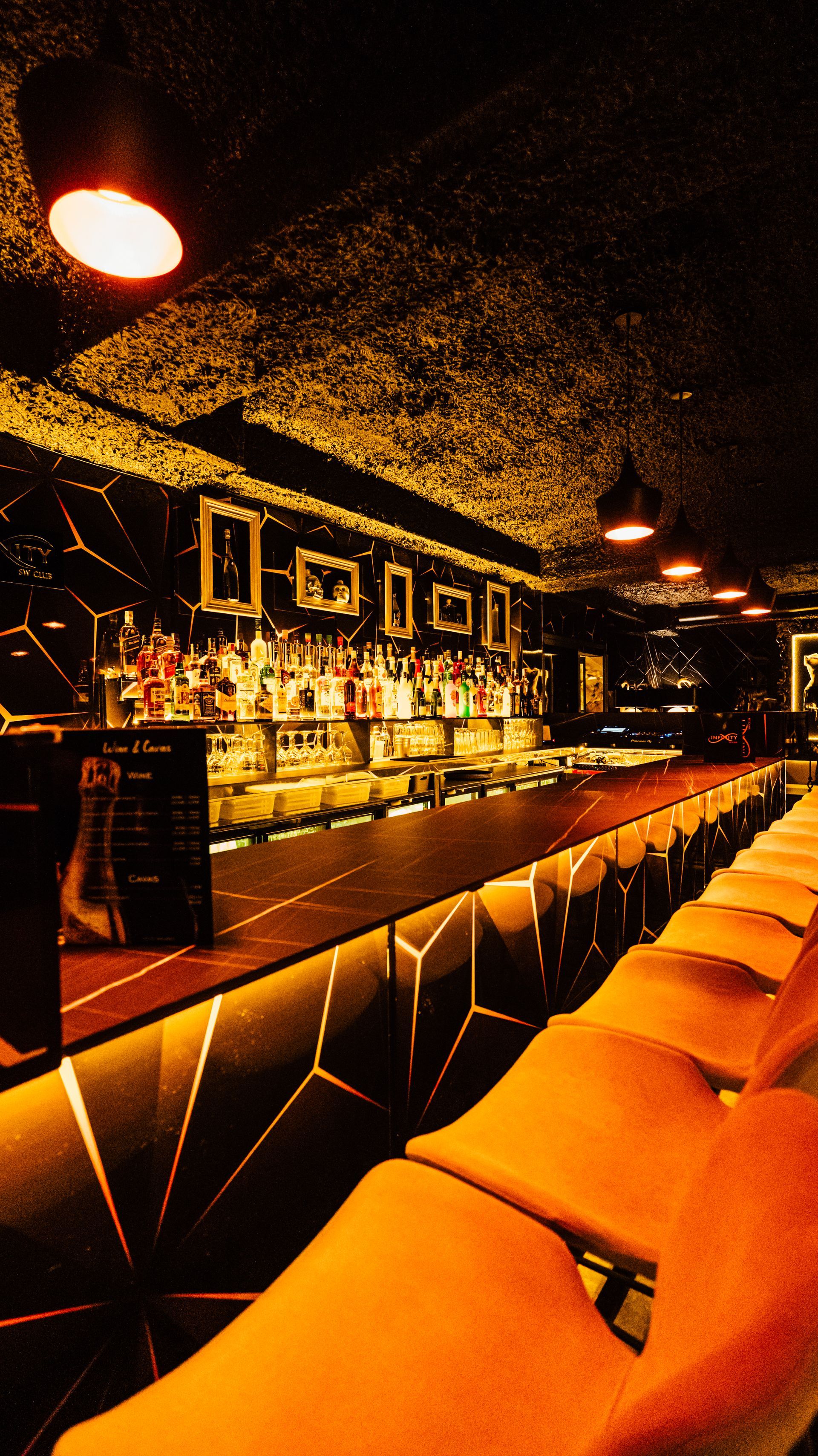 Warmly lit empty bar interior with orange stools, dark walls, and hanging lamps