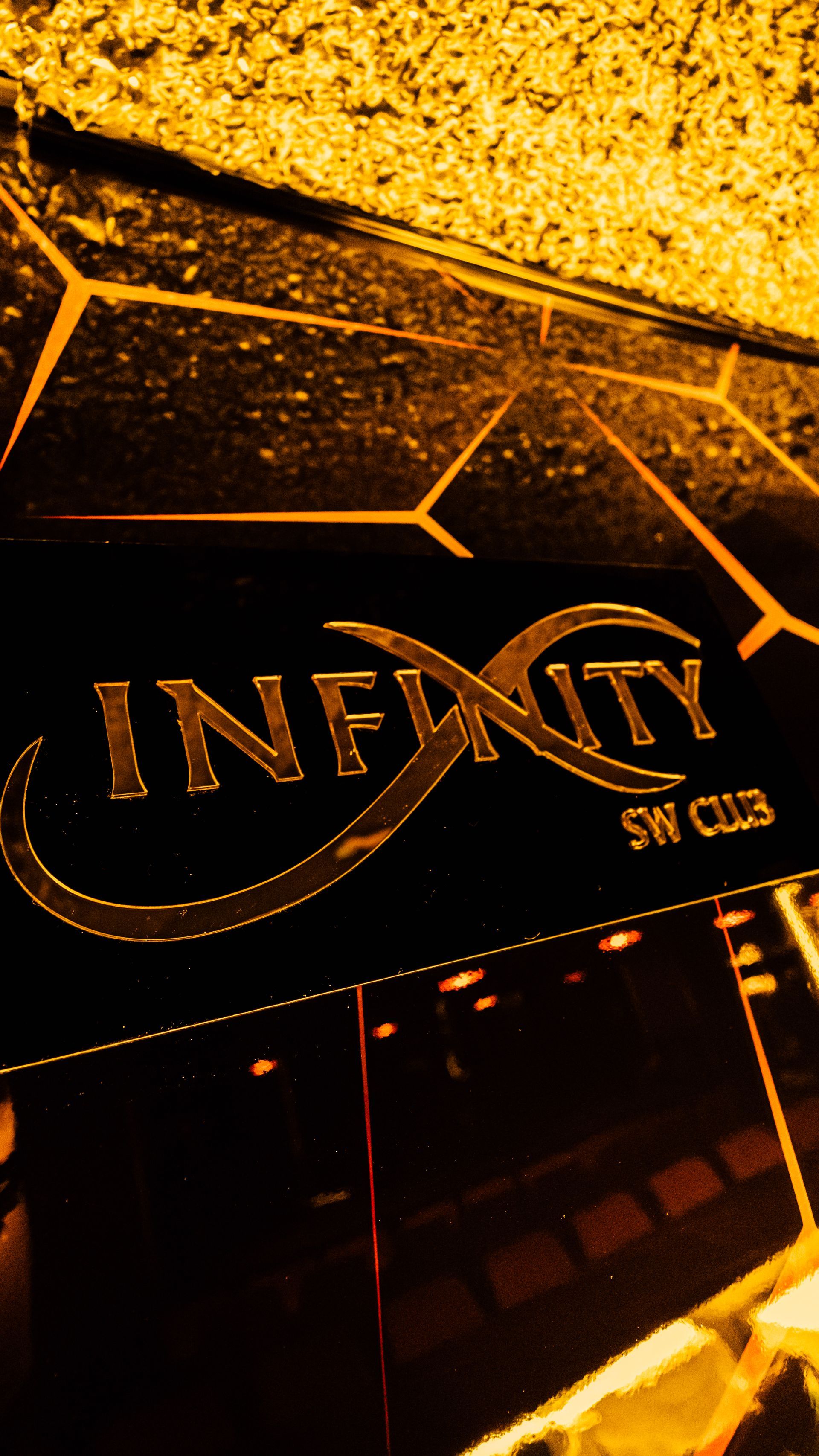 Close-up of a glowing gold Infinity sign on a dark, geometric surface.