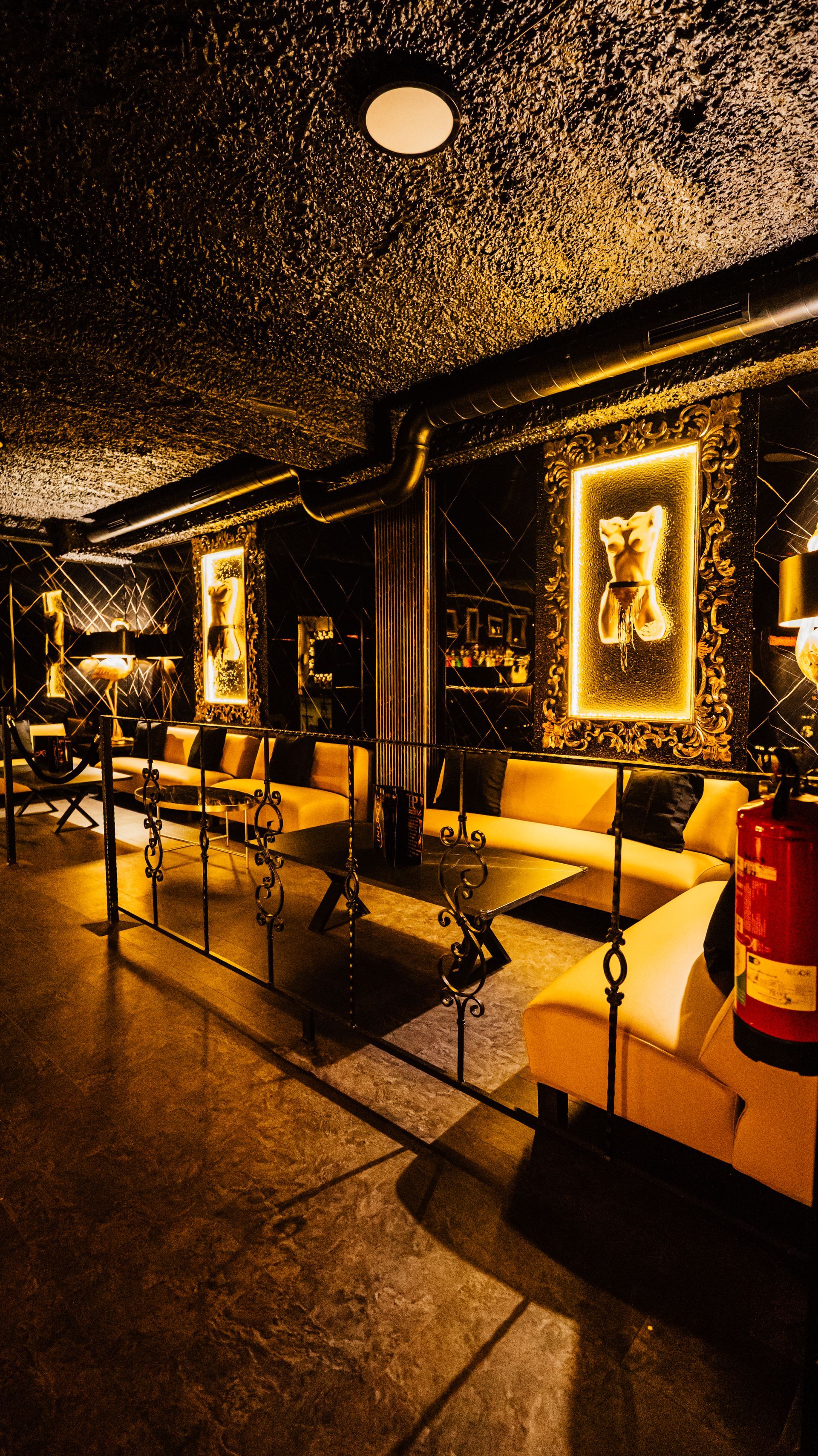 Warmly lit elegant lounge with dark decor, framed art, seating, and a reflective polished floor.