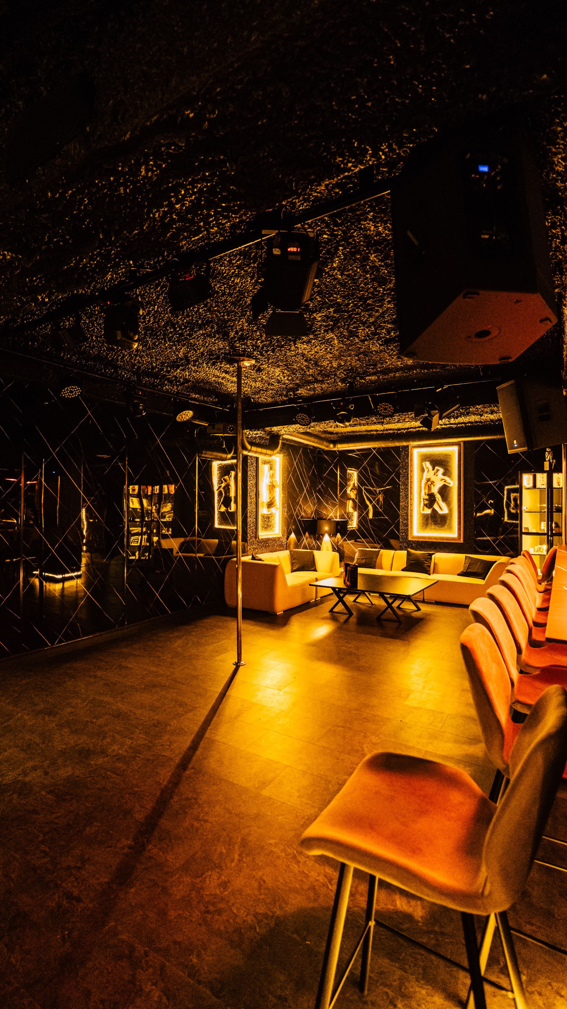 Warmly lit lounge with orange chairs, glowing tables, and a starry ceiling at night