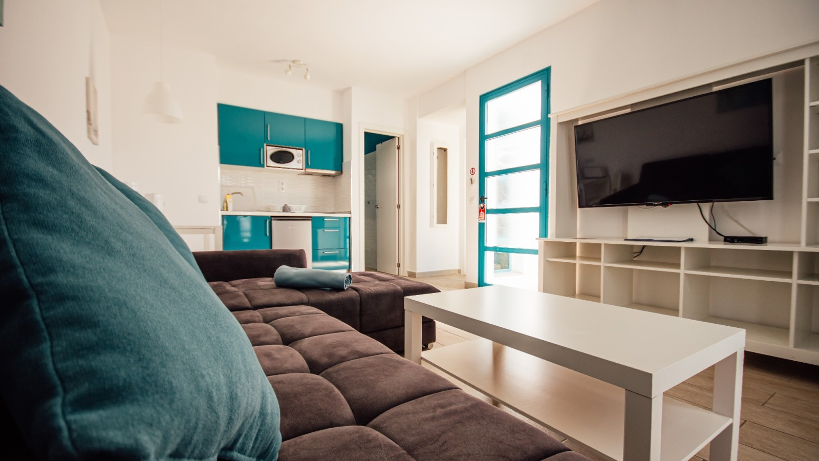 Modern living room with teal accents, gray sofa, white coffee table, and wall-mounted TV