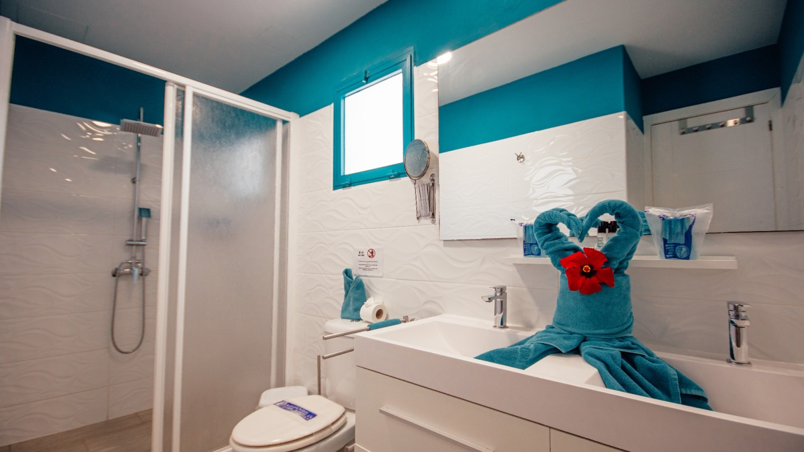 Bright bathroom with shower, sink, and a blue teddy bear holding red flowers on the counter