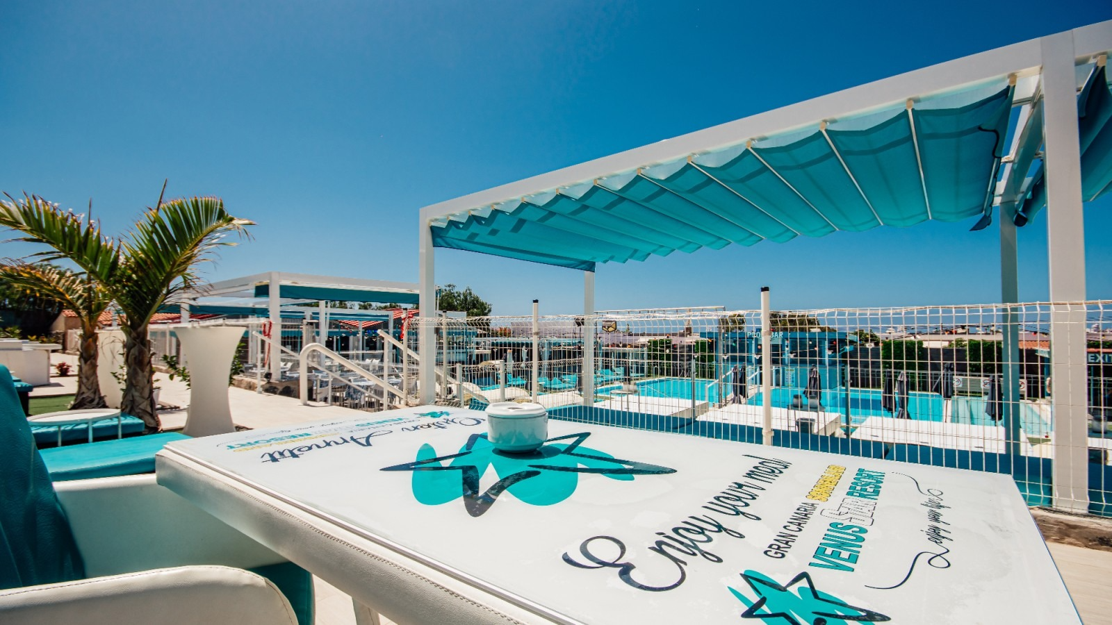 Sun loungers under a turquoise canopy beside a sunny pool overlooking the marina