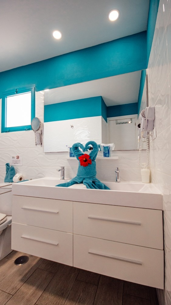 Blue stuffed toy on a white bathroom sink in a bright modern bathroom with teal accents