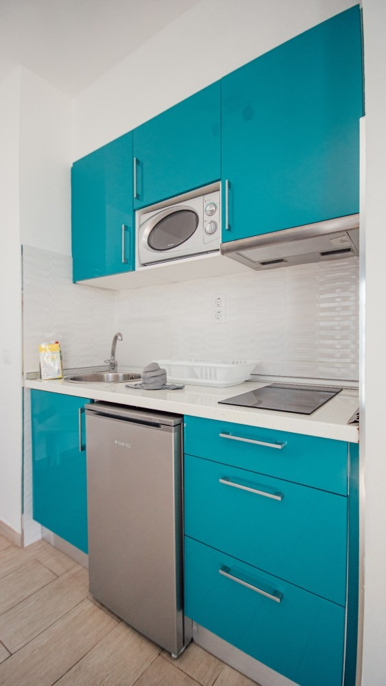 Modern teal kitchen with stainless steel appliances, white countertop, and built-in microwave above stove.