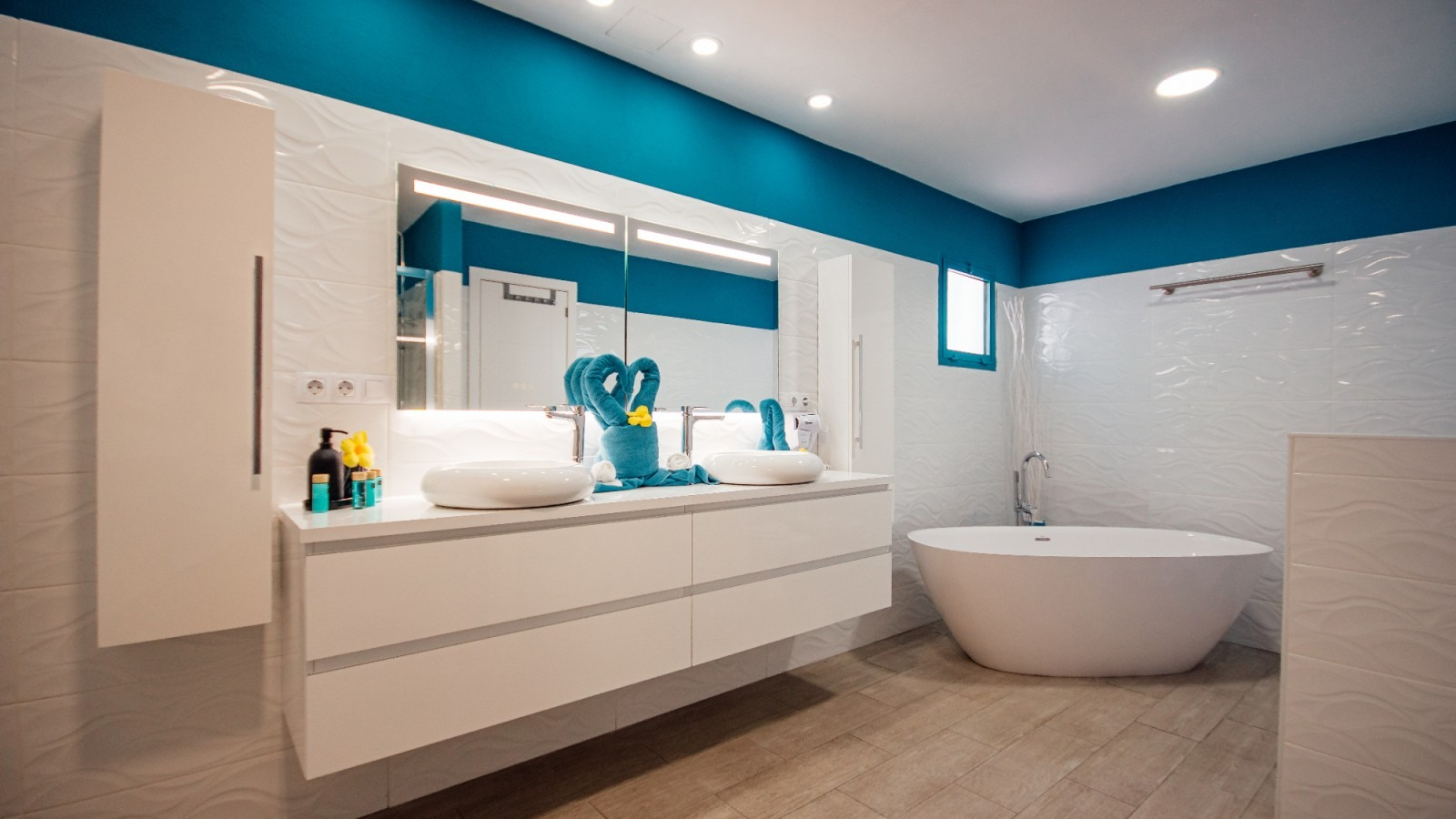 Modern white bathroom with teal accents, double vanity, mirror, tub, and light wood flooring