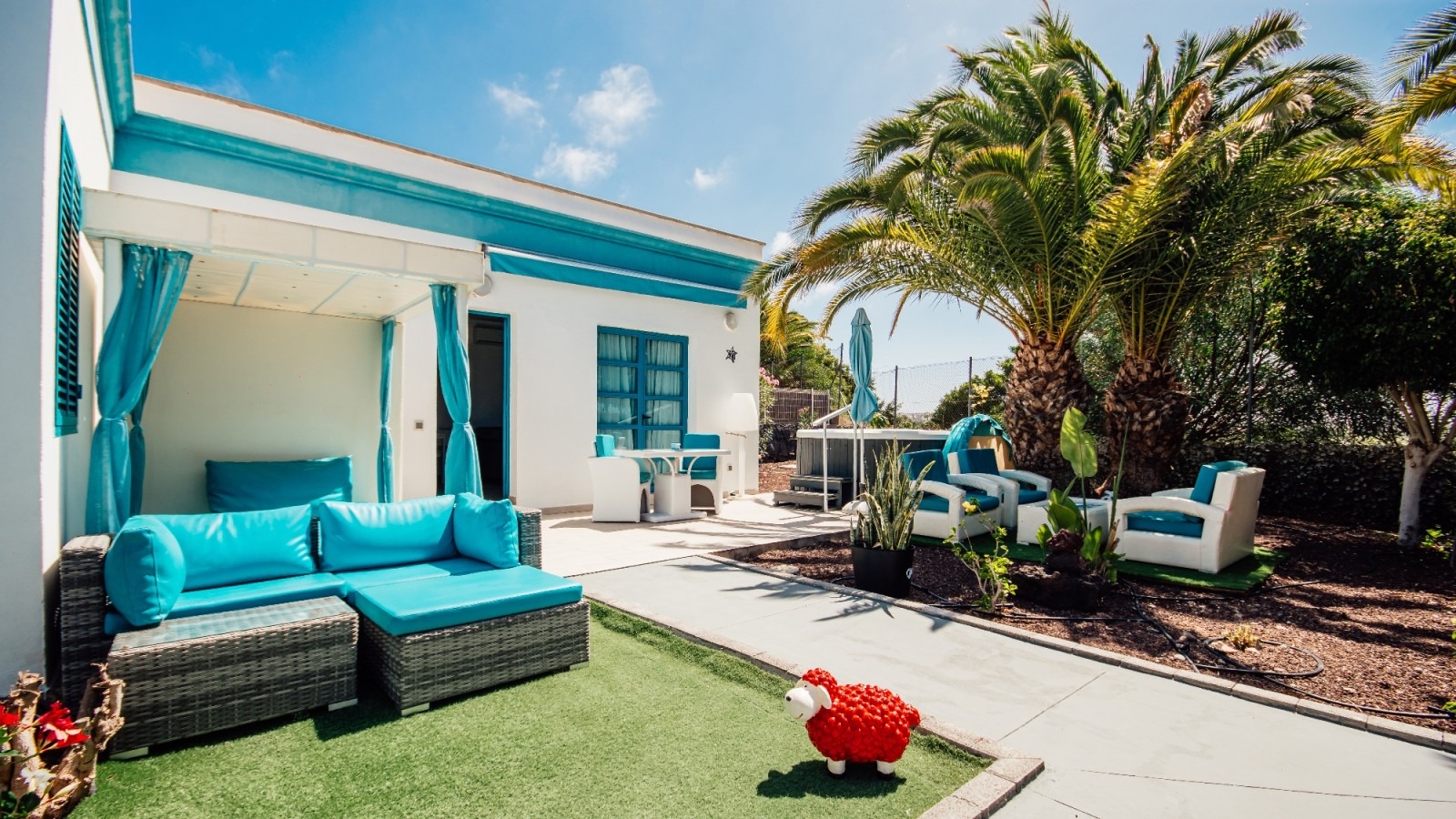 Turquoise patio with wicker sofa, white lounge chairs, and palm tree in a sunny backyard