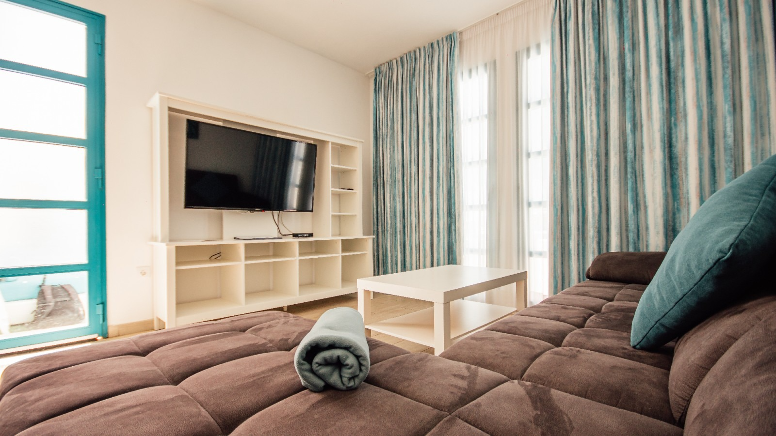 Bright living room with brown sofa, TV wall unit, striped curtains, and a window