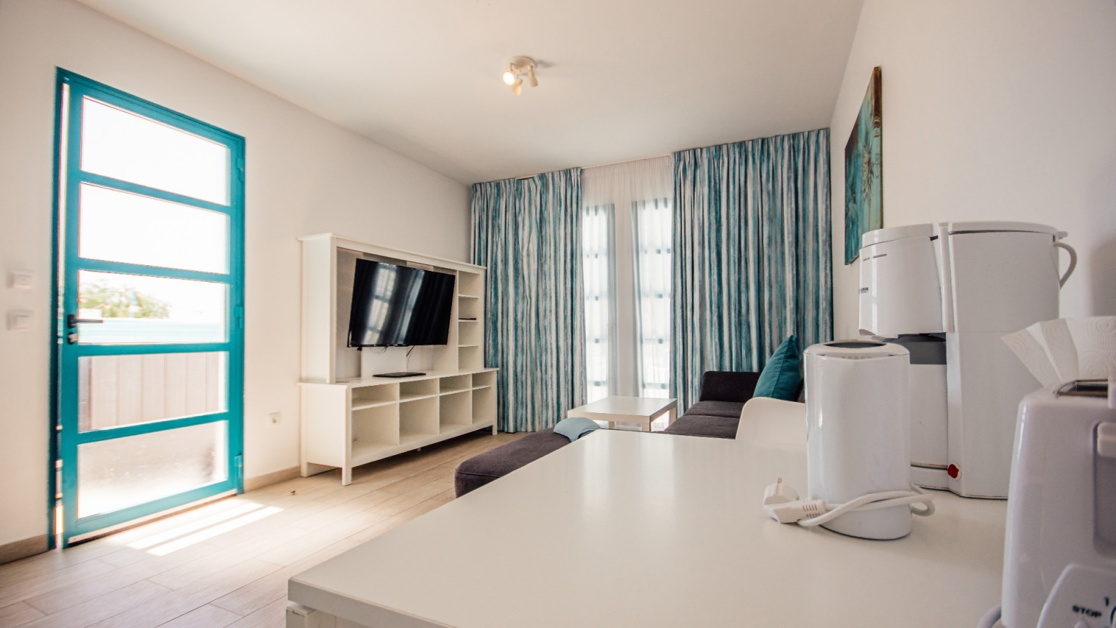 Bright hotel-style room with twin beds, blue curtains, TV, and large windows.