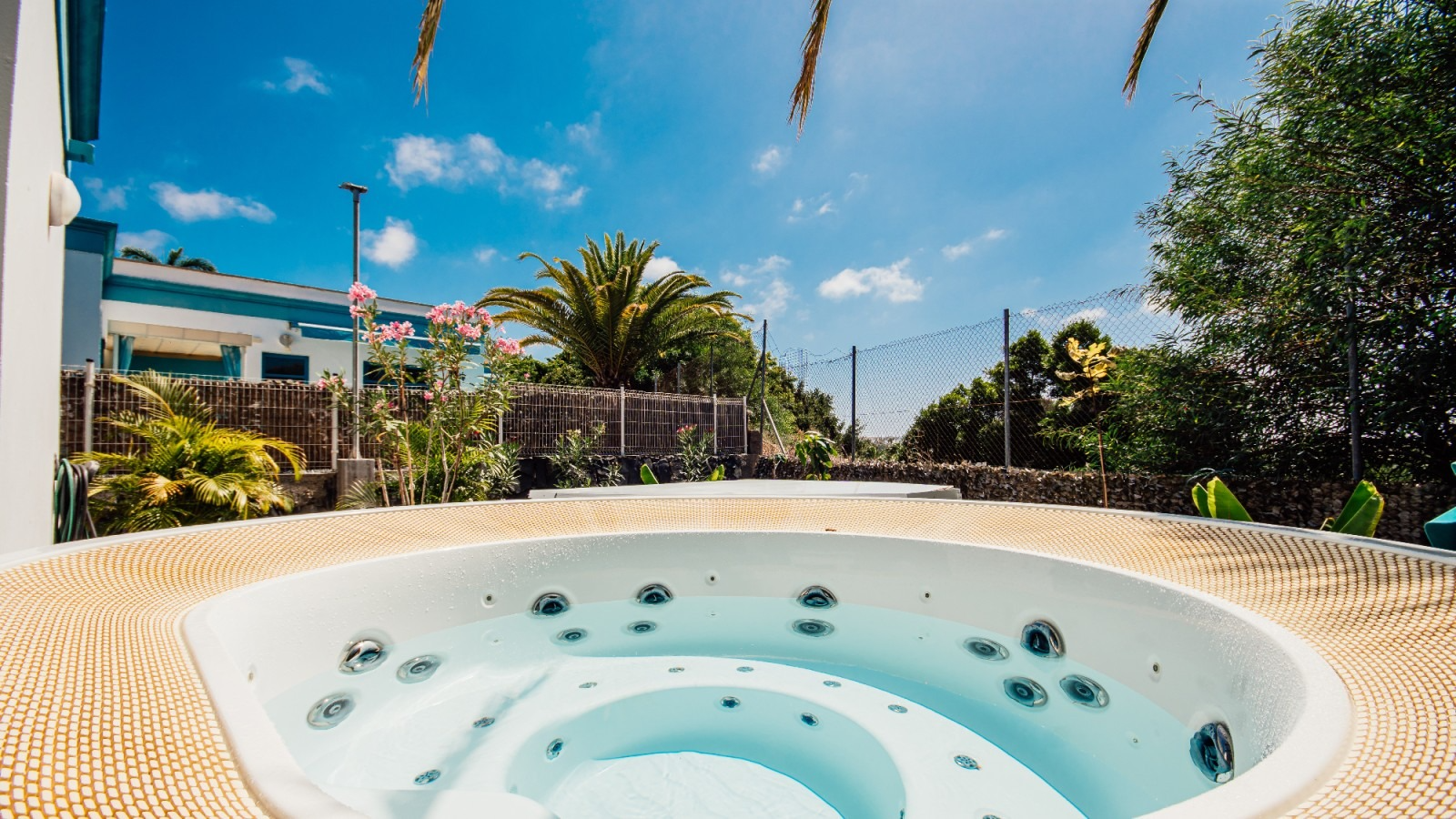 White outdoor hot tub with clear blue water in a sunny tropical backyard with palm trees and blue sky