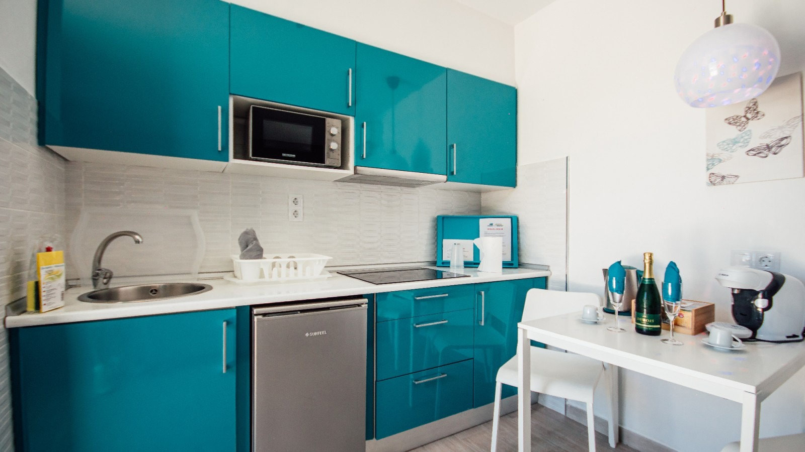 Turquoise kitchen with white cabinets, stainless appliances, and a small dining table with bottles.