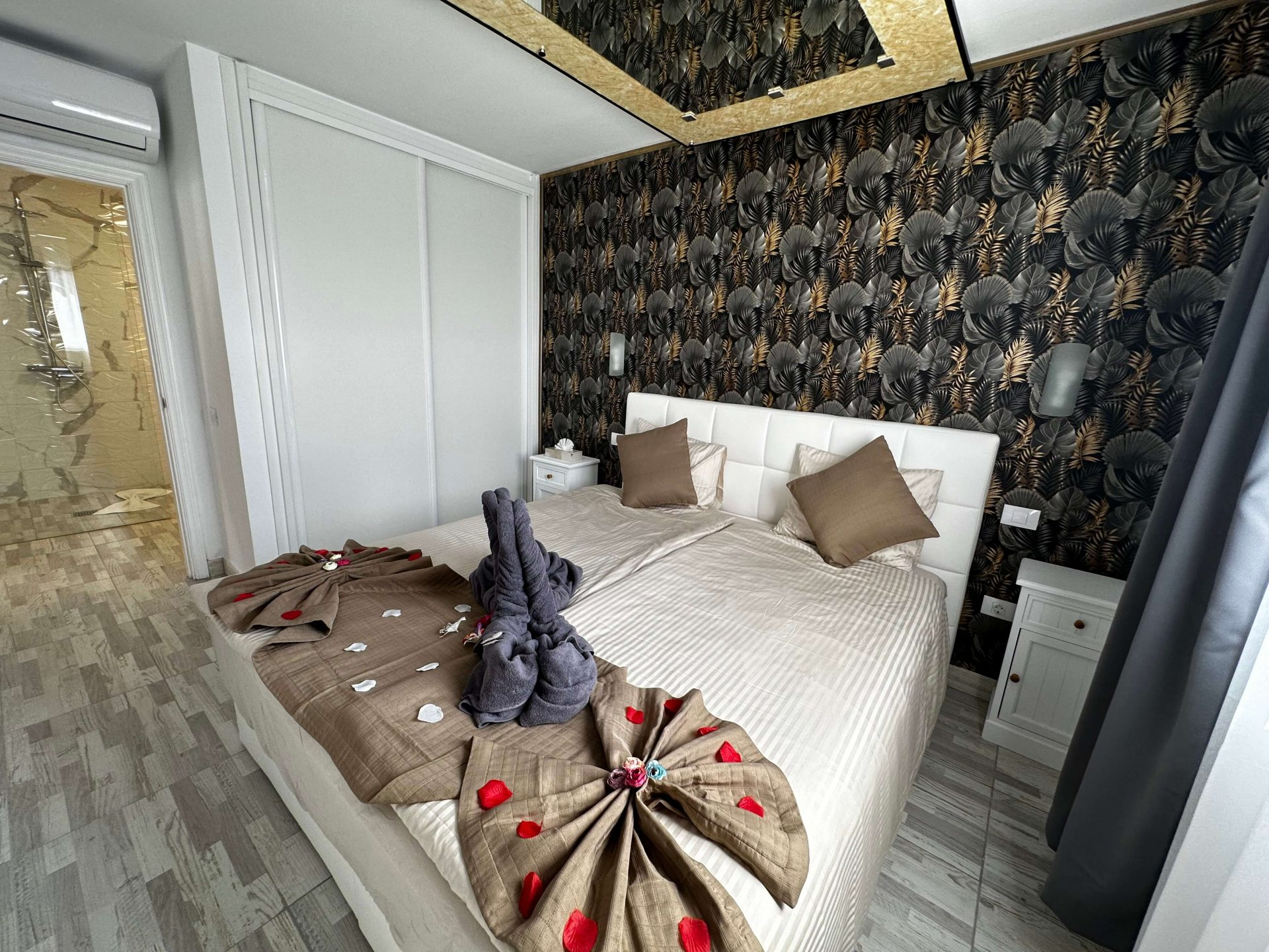 Modern bedroom with white bed, patterned black wallpaper, and gray curtains