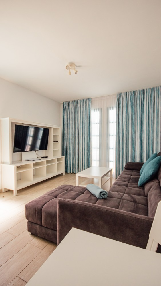 Bright living room with a brown sectional sofa, TV stand, and blue curtains by a glass door.