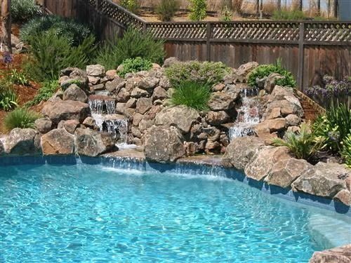 Backyard pool with bright blue water and a rocky waterfall landscaped with greenery