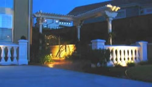 Illuminated driveway entrance with white pillars and a lit archway at dusk