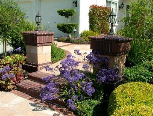 Flower-lined brick garden steps and pillars leading to a white house entrance