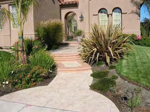 Front yard walkway to a stucco house with desert plants and a green lawn
