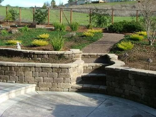 Landscaped backyard with stone retaining walls, steps, and a winding path through shrubs and flowers