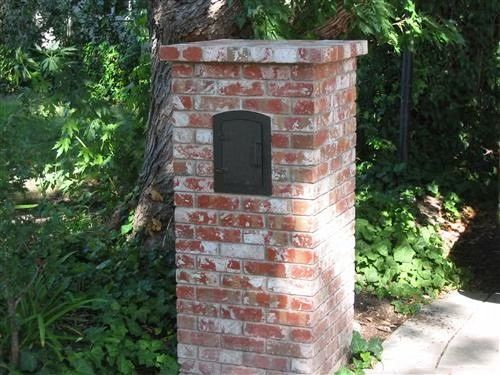 Brick pillar with a dark plaque beside a tree and garden path