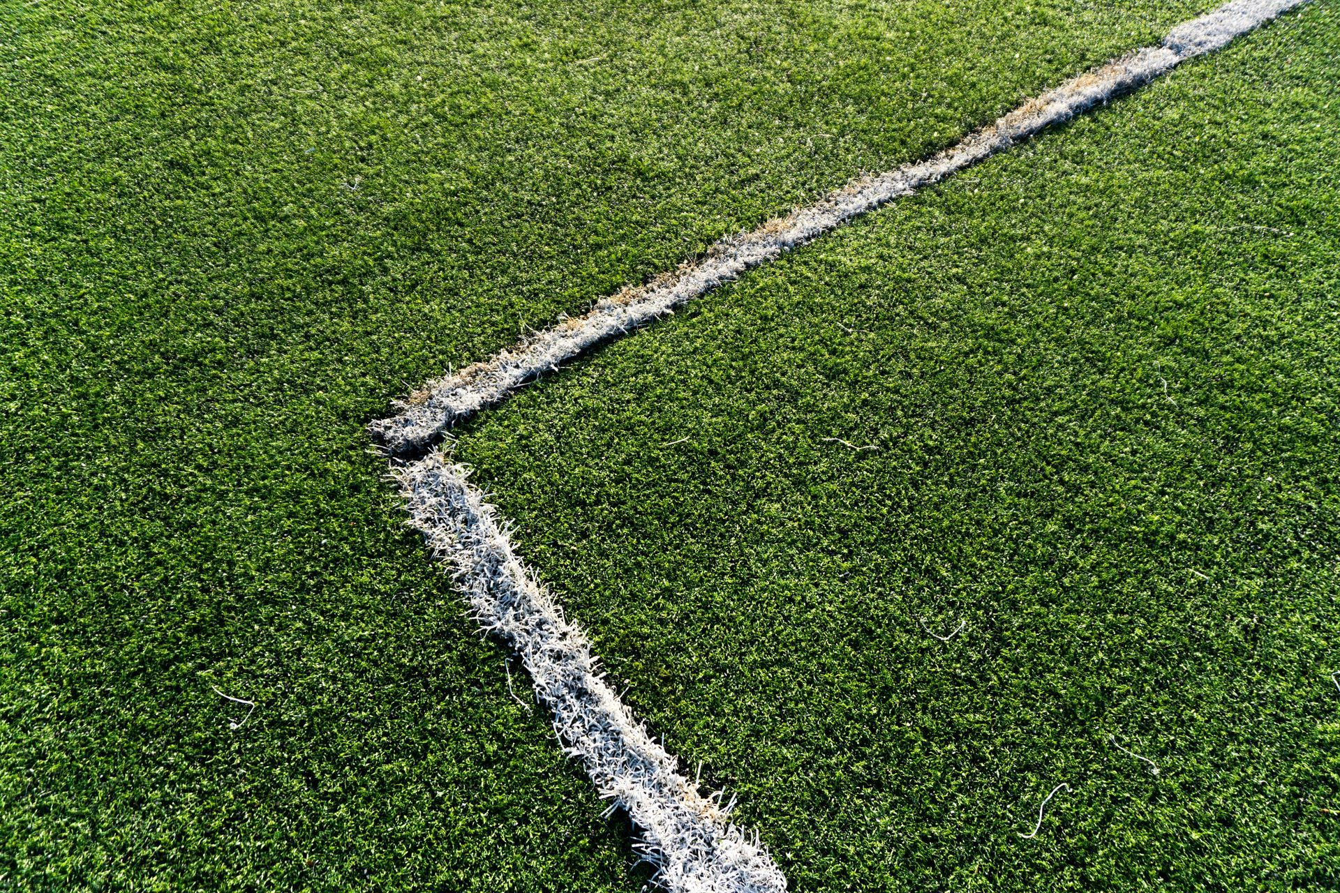 A corner section of white boundary lines marked on a bright green artificial turf field.