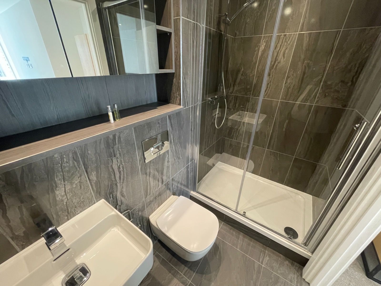 Modern bathroom with a shower, toilet, and sink. Dark grey tile, glass shower door.