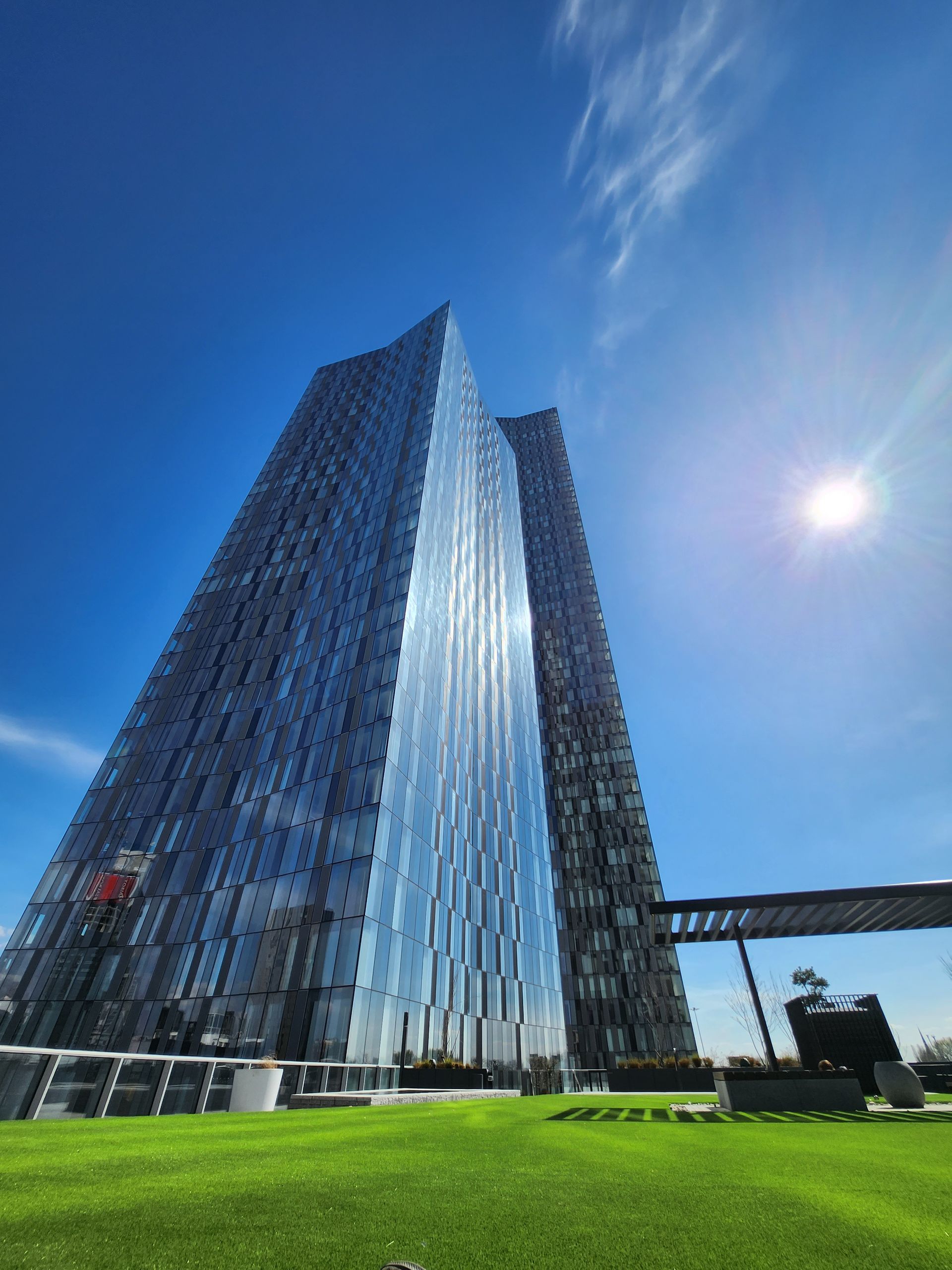 Tall glass skyscraper against a bright blue sky with a green lawn in the foreground.