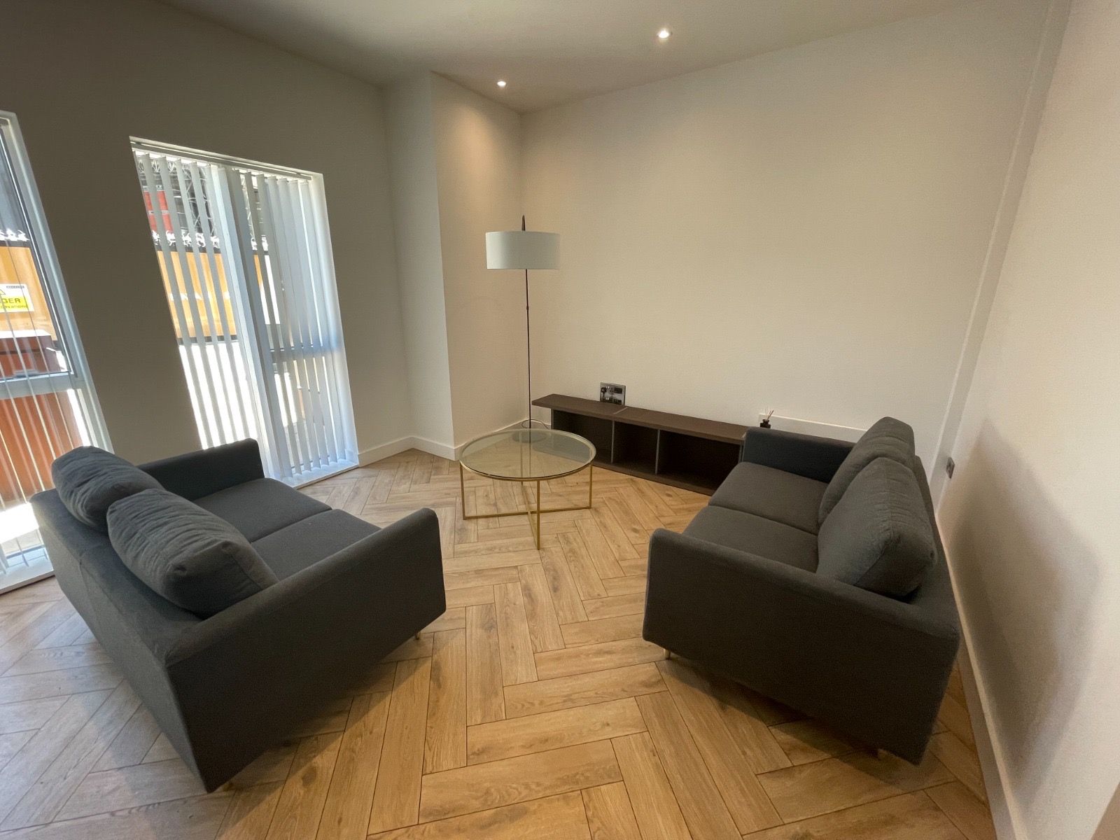 Living room with two gray sofas, glass coffee table, and media console on herringbone floor.