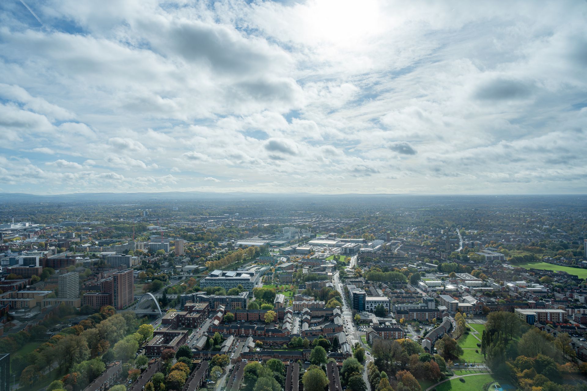 Aerial view of a city with buildings, roads, and trees under a cloudy sky.