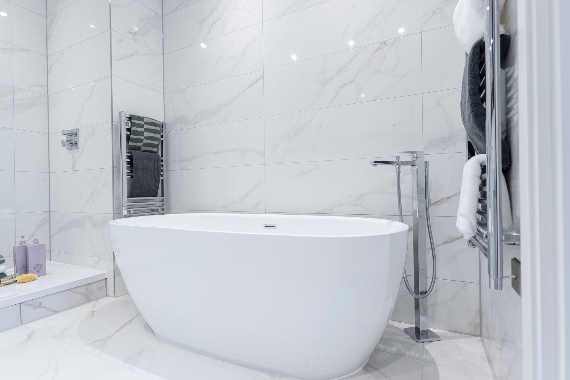 White, modern bathroom with a freestanding tub. Marble tile walls and floor, chrome fixtures.