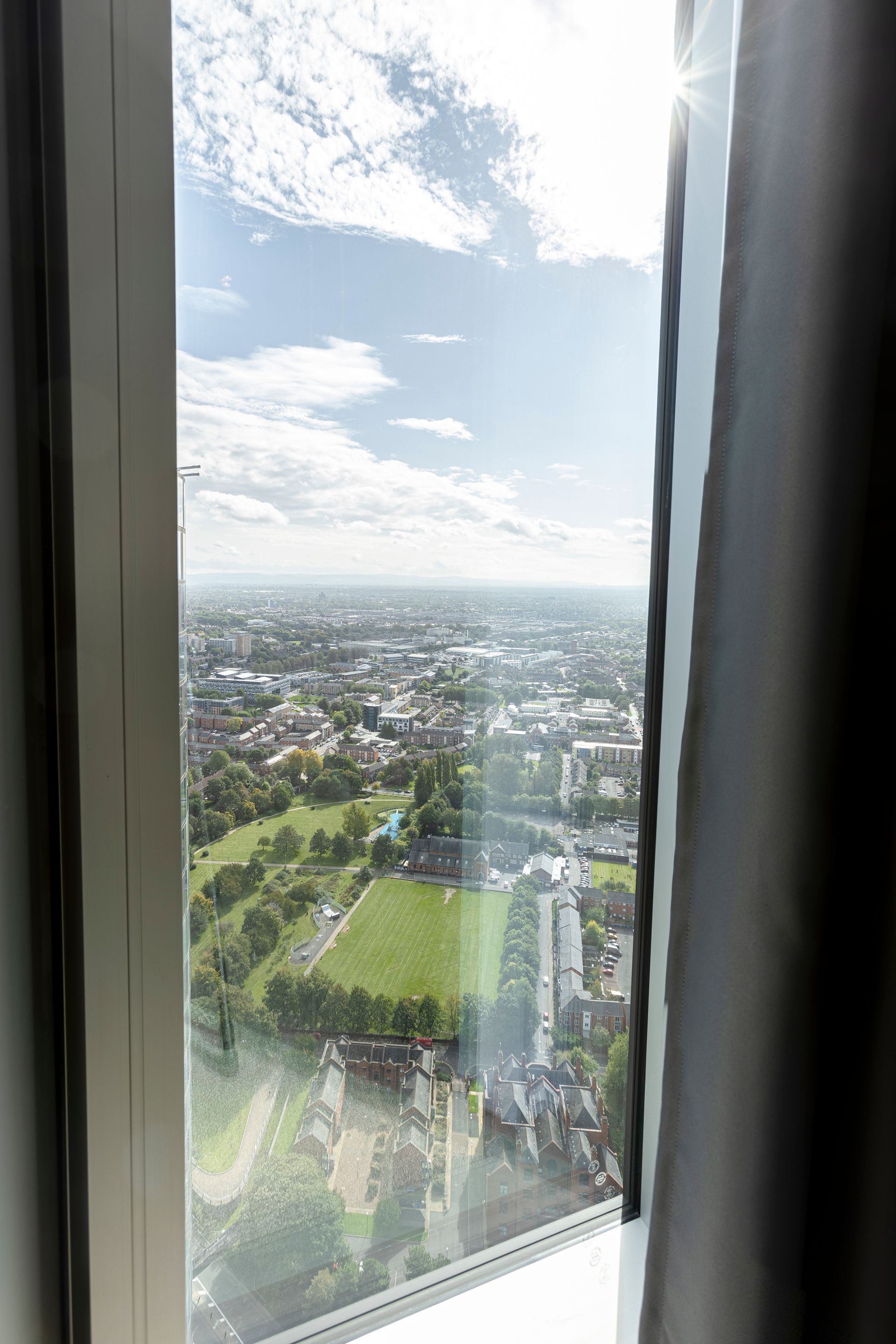 View from a high window, overlooking a city and park with blue sky and white clouds.