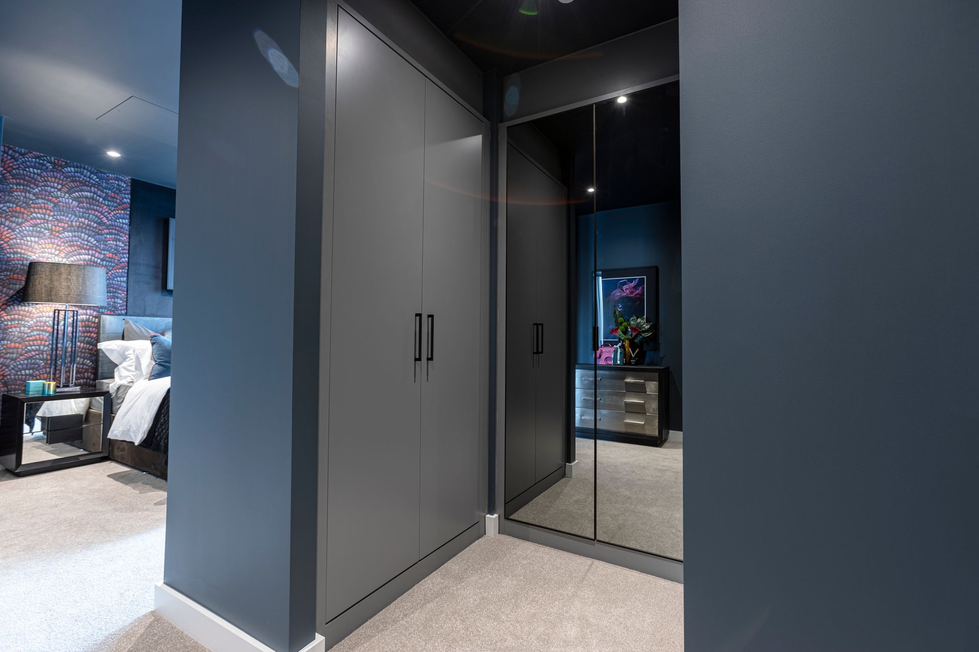 Dark gray wardrobe with mirrored wall, hallway leads to a bedroom with dark blue walls.