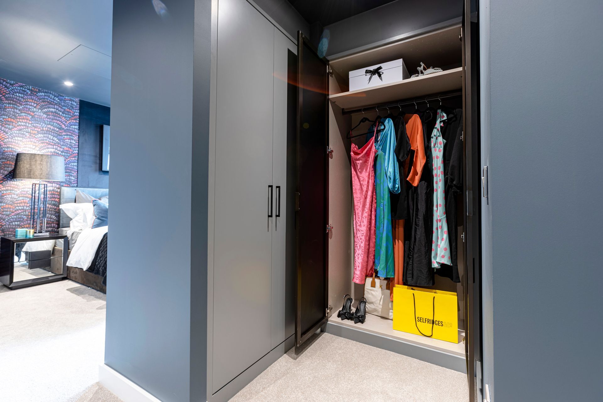 Closet with open door revealing clothes on hangers and shelves with items. Gray and black interior.