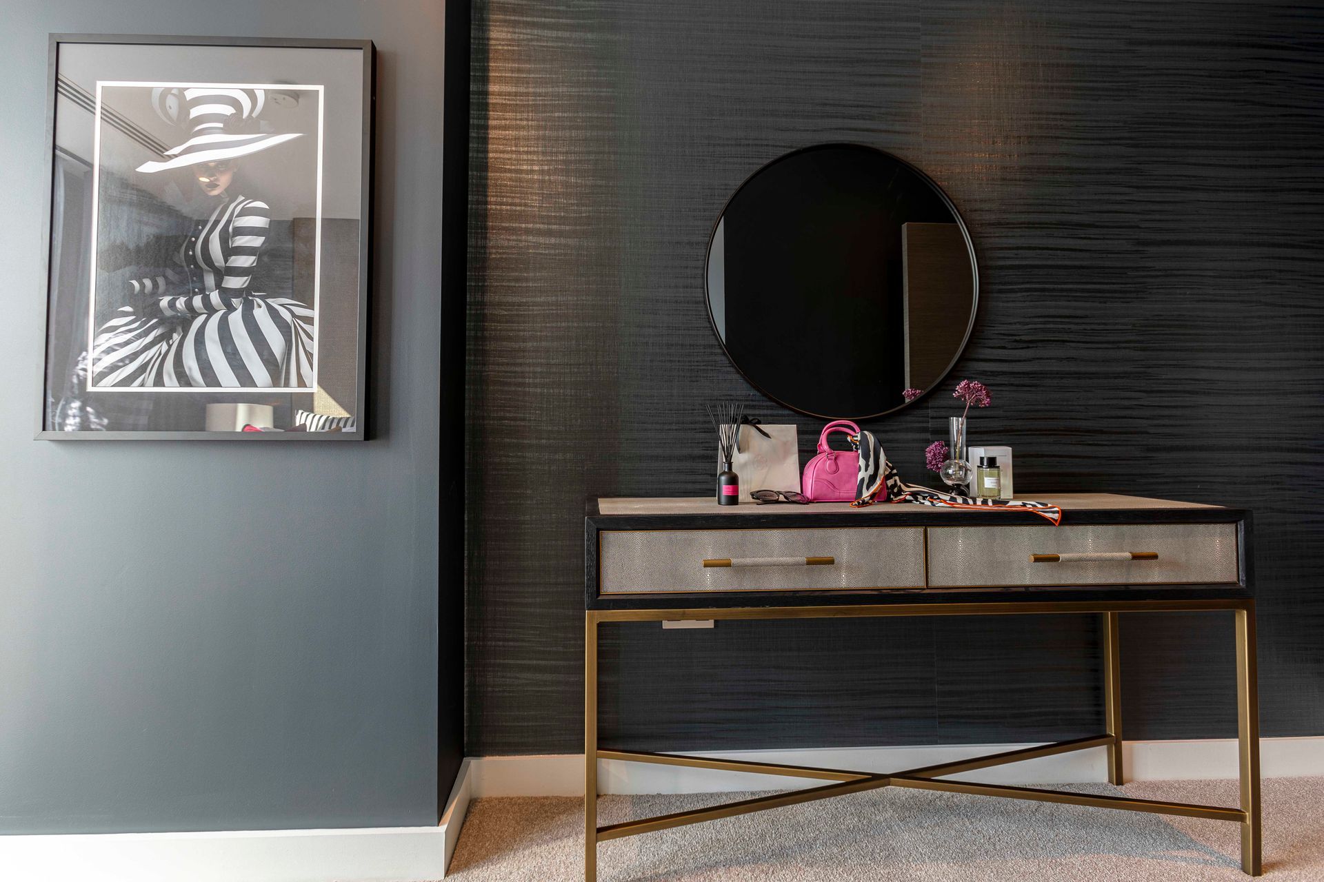 Vanity with mirror, art, and decor against a dark, textured wall.