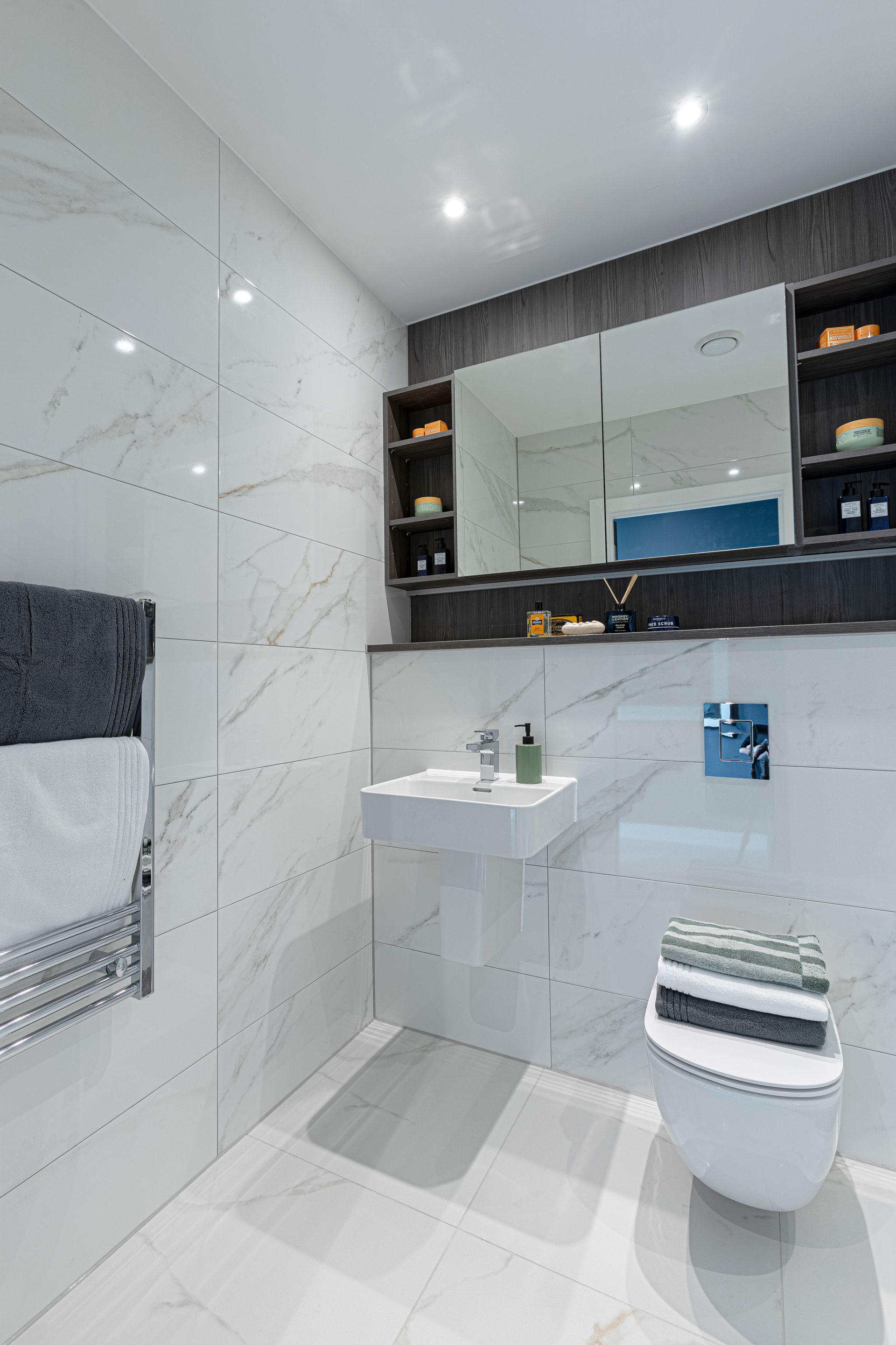 Modern white bathroom with marble tiles, floating sink, toilet, and mirrored cabinet.