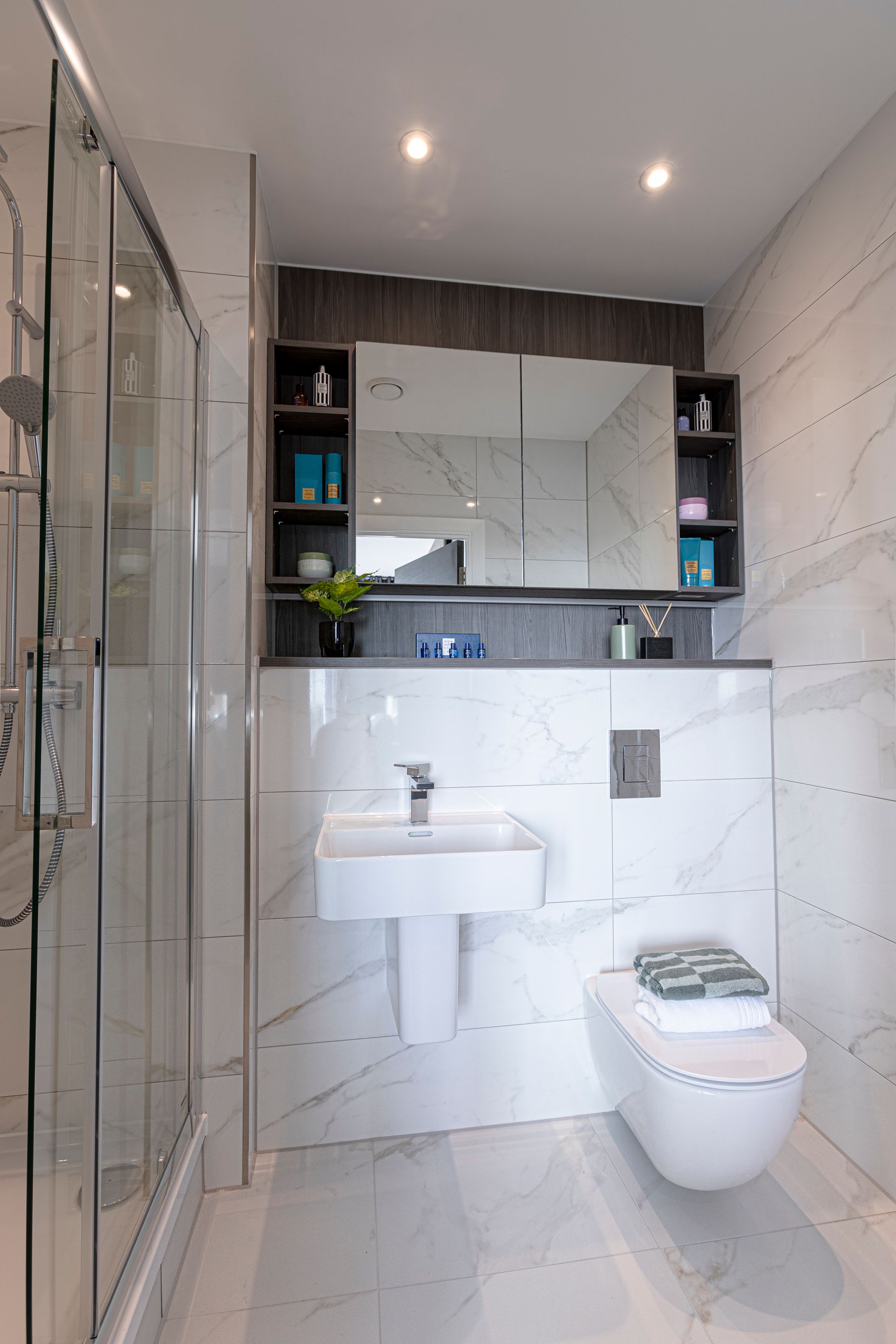 Modern bathroom with marble-look tile. Features a shower, sink, wall-mounted toilet, and mirrored cabinet.