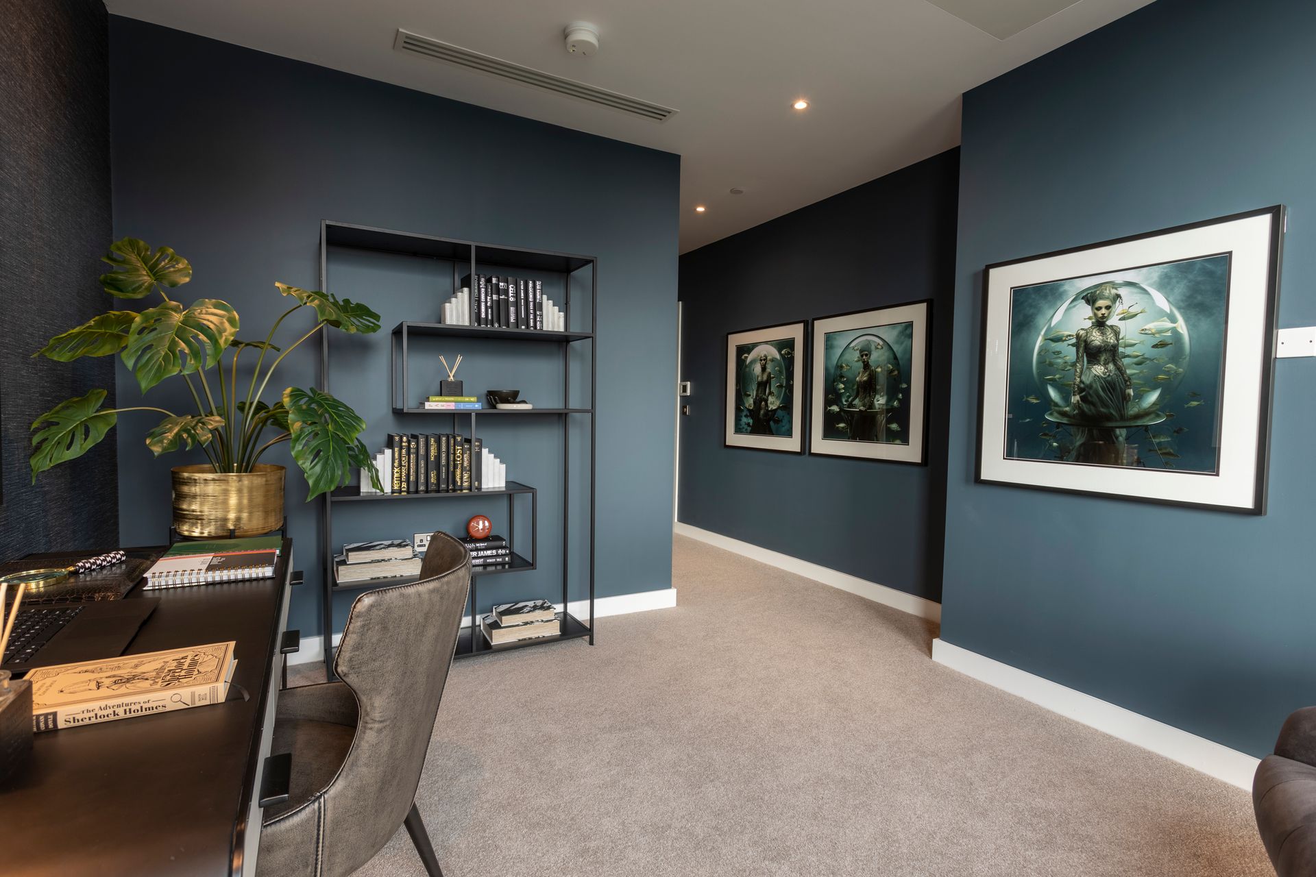 Home office with blue walls, framed art, a desk with a plant, and a metal bookshelf.