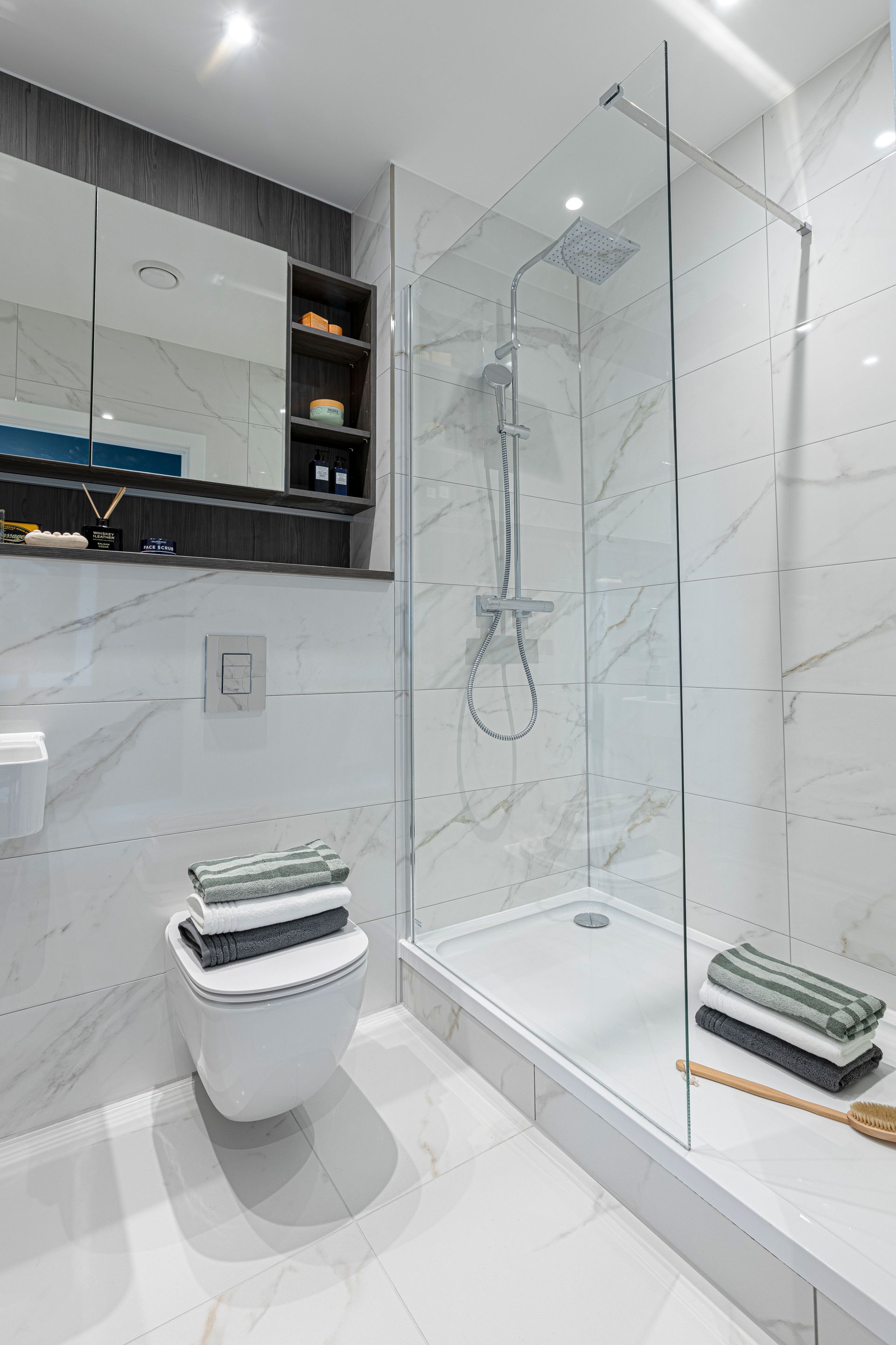 Modern bathroom with marble walls, glass shower, toilet, and towels.