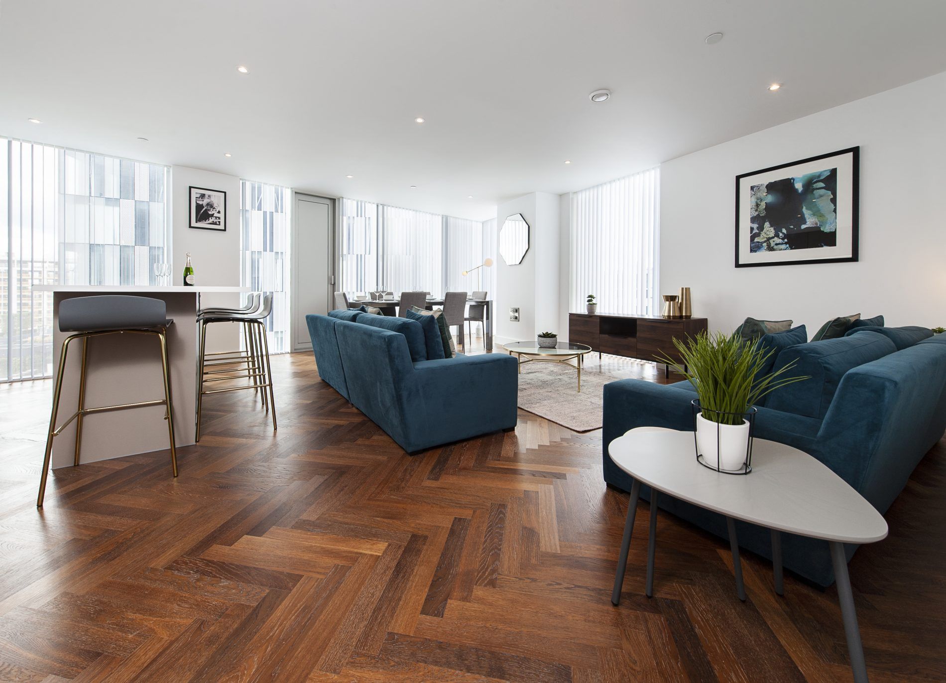 Spacious, modern living room with blue sofas, wooden floors, and a city view.