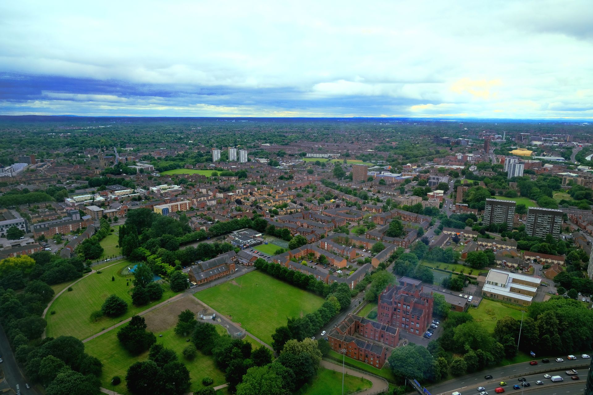 Aerial view of a town with residential buildings, green spaces, and a cloudy sky overhead.