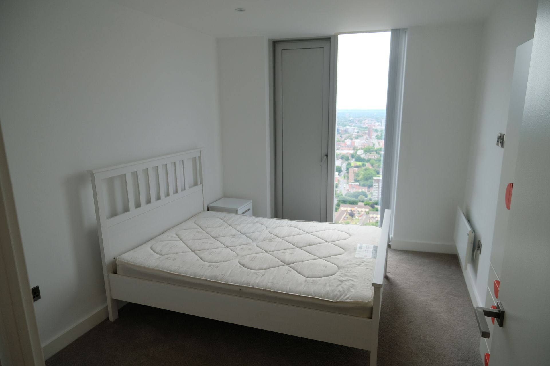 White bedroom with bed, nightstand, tall window, and closet.