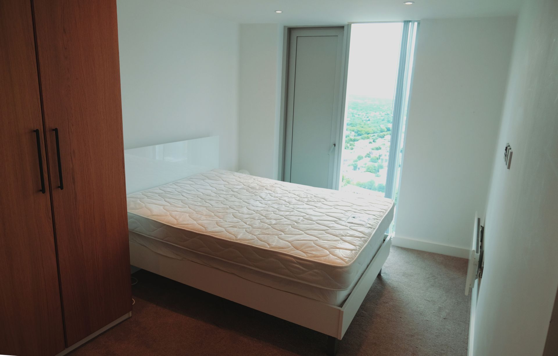 Bedroom with bed, wardrobe, and window overlooking trees.