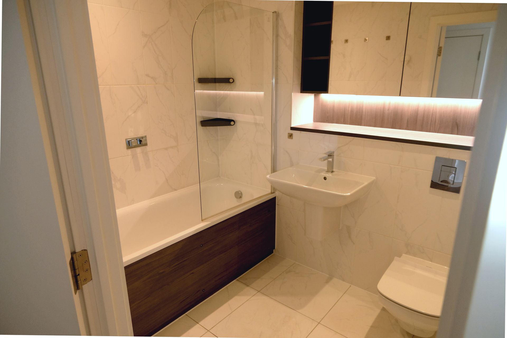 Small bathroom with bathtub, sink, and toilet; white and wood tones.