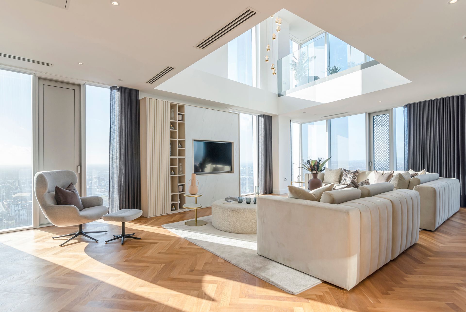 Bright, modern living room with large windows, light-colored furniture, hardwood floors, and a skylight.